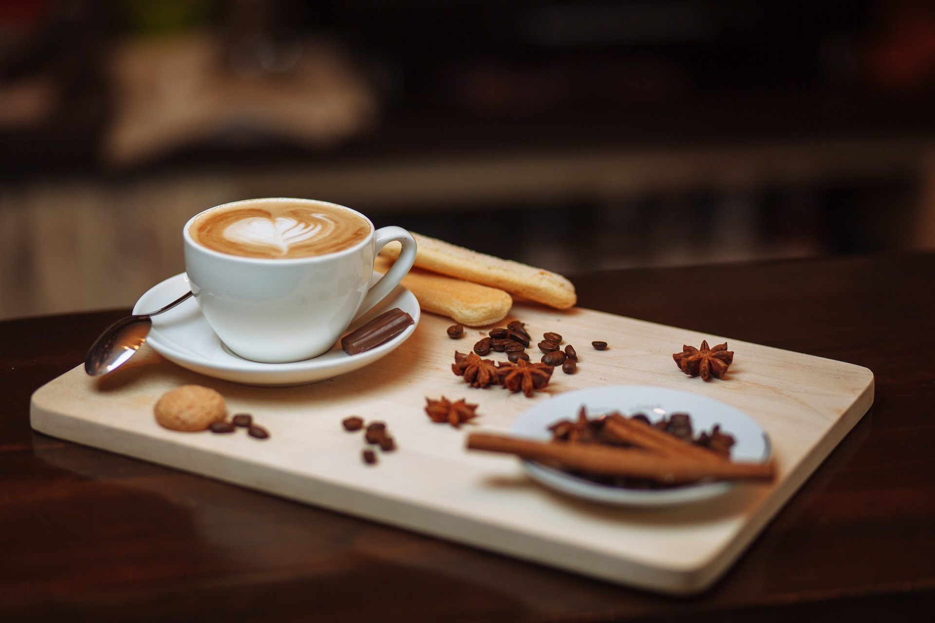 A cup of coffee placed in a saucer and spices scattered around on a flat tray. 